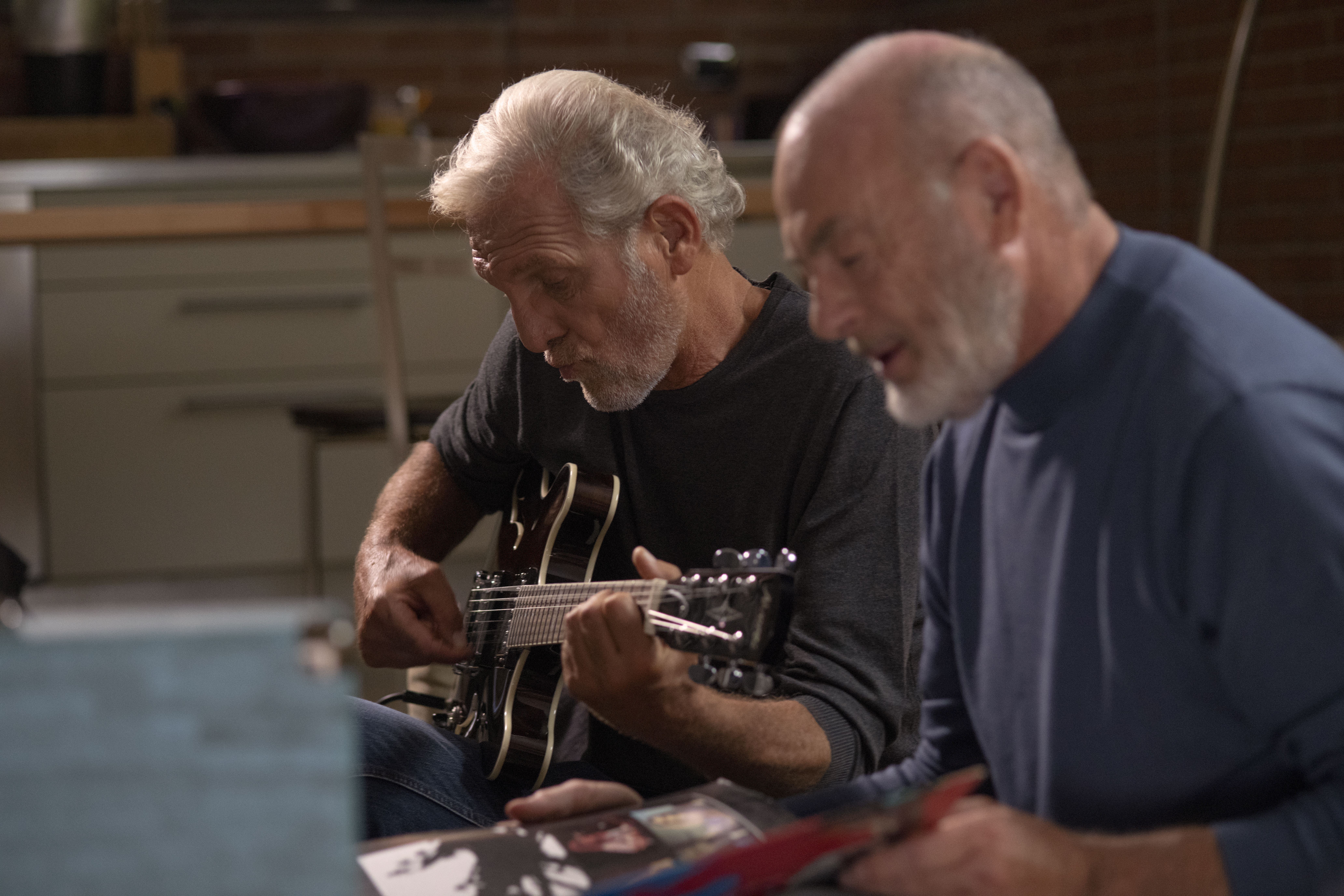 Freunde sitzen auf einem Sofa und spielen Gitarre.